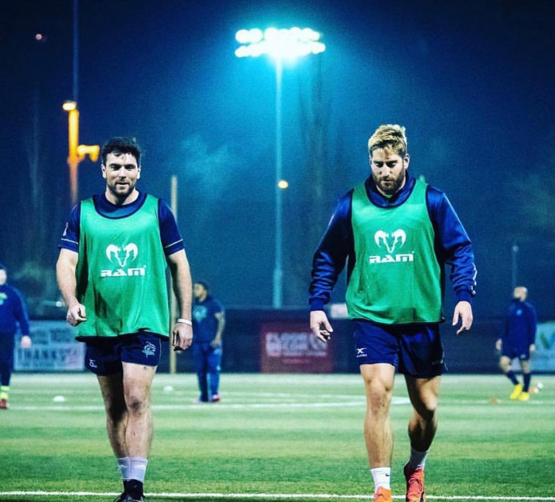 Rugby players wearing green RAM training bibs under floodlights
